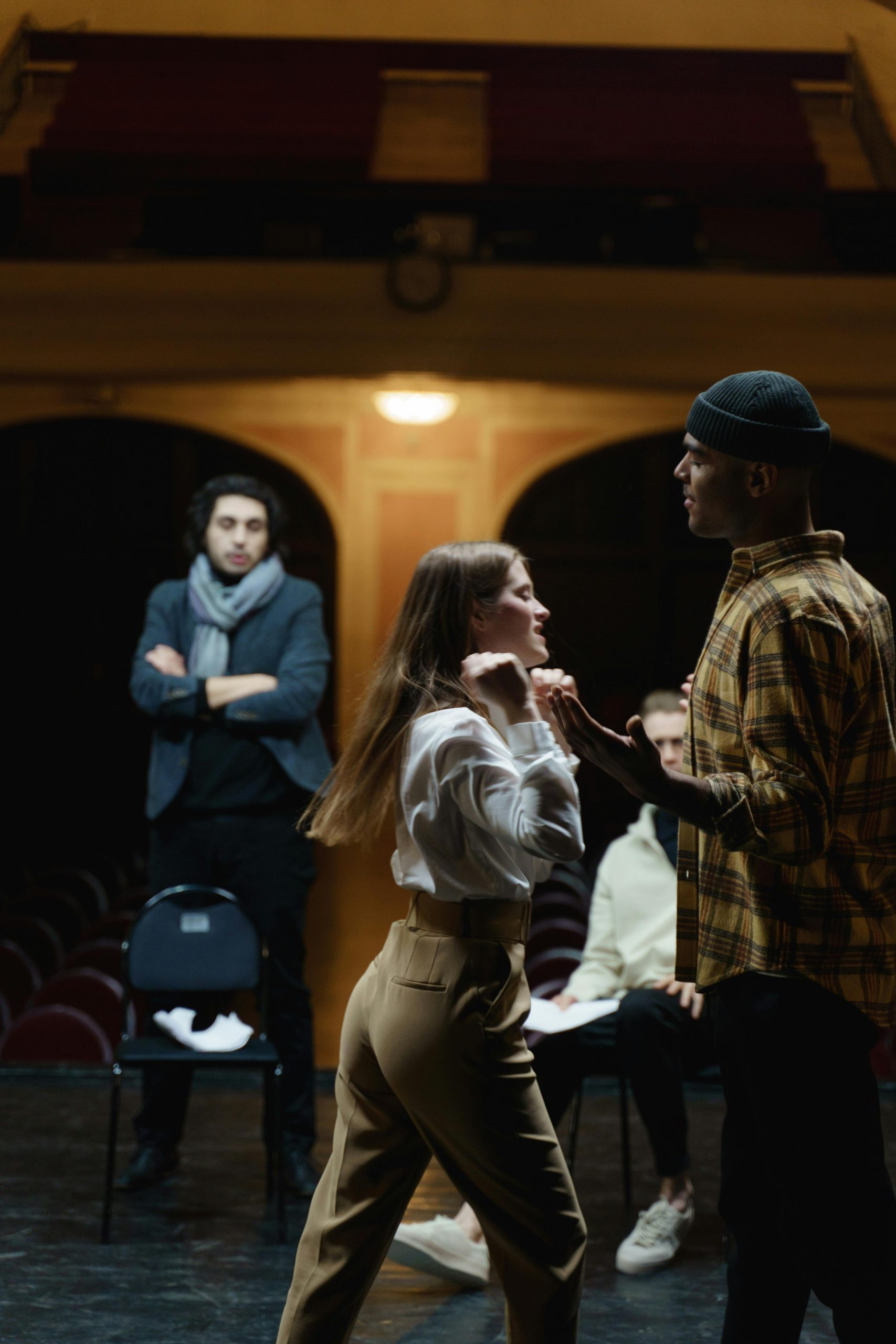 Actors rehearsing an intense scene on stage with a director observing in a theater setting.